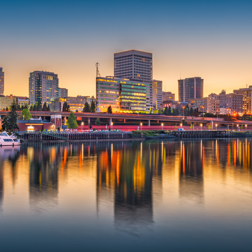 Evening cityscape of Tacoma, Washington, viewed from across the Thea Foss Waterway with high-rise buildings glowing under the sunset and their reflections mirrored in the water, representing the urban area near Yakima Hill where you can find a dispensary near Yakima Hill.